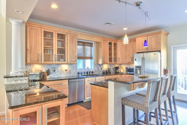 kitchen with stainless steel appliances, light wood-style flooring, a sink, a breakfast bar, and dark stone counters