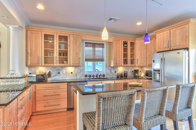 kitchen featuring a sink, appliances with stainless steel finishes, glass insert cabinets, a breakfast bar, and recessed lighting