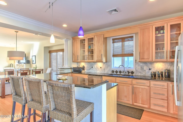 kitchen with a sink, light wood-style flooring, a kitchen bar, crown molding, and decorative backsplash