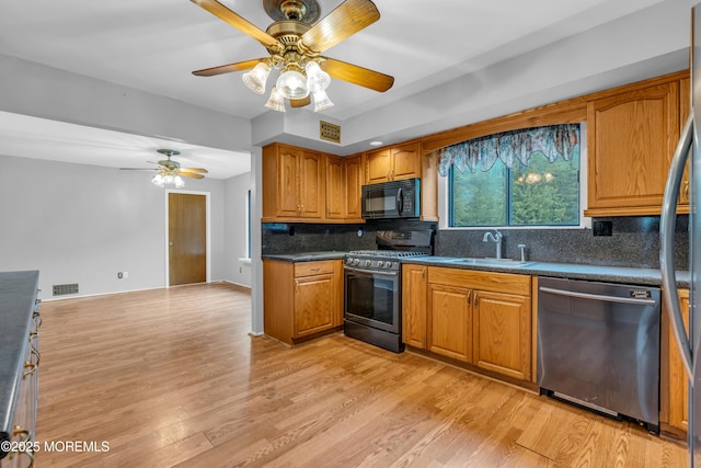 kitchen with appliances with stainless steel finishes, a sink, brown cabinetry, a ceiling fan, and light wood-type flooring