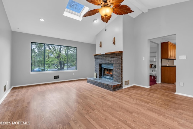 unfurnished living room with high vaulted ceiling, a fireplace, ceiling fan, light wood-style floors, and a skylight