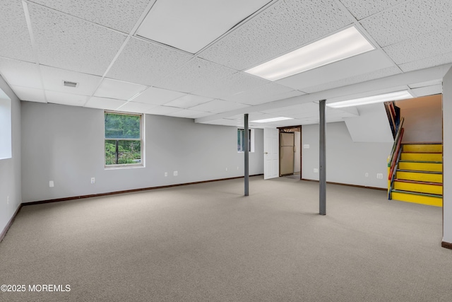 basement with a drop ceiling, baseboards, light colored carpet, and stairway