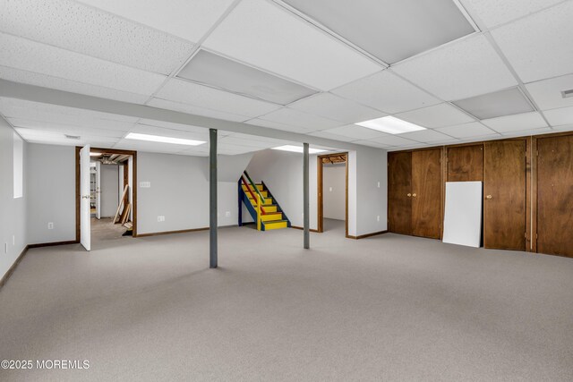 finished below grade area featuring a drop ceiling, stairs, baseboards, and light colored carpet