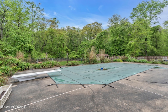 view of swimming pool with a patio area, fence, and a wooded view