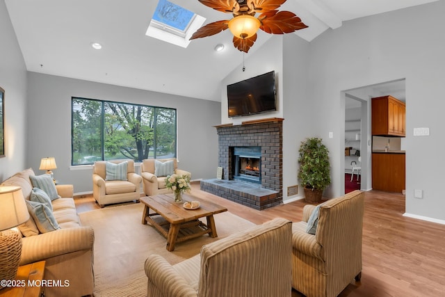 living area with ceiling fan, high vaulted ceiling, light wood finished floors, a brick fireplace, and baseboards