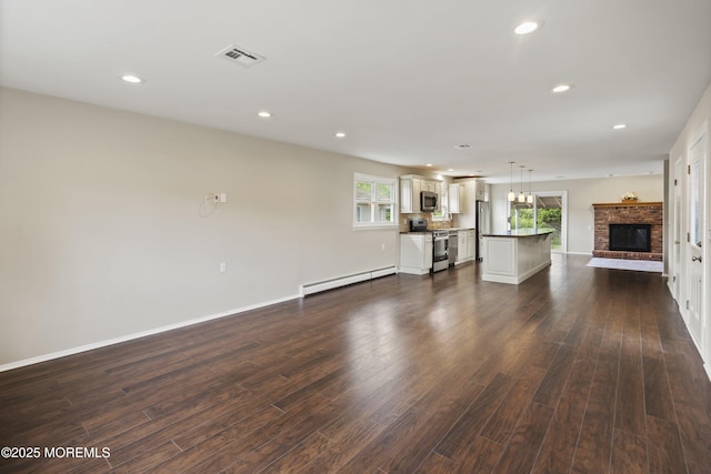 unfurnished living room with baseboard heating, healthy amount of natural light, dark wood-type flooring, and recessed lighting