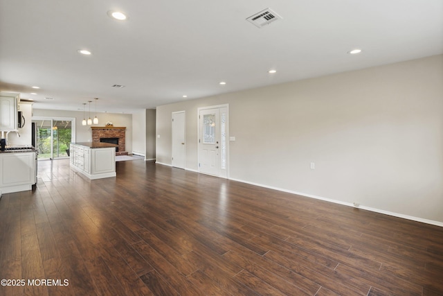 unfurnished living room featuring a fireplace, dark wood-type flooring, recessed lighting, baseboards, and a sink