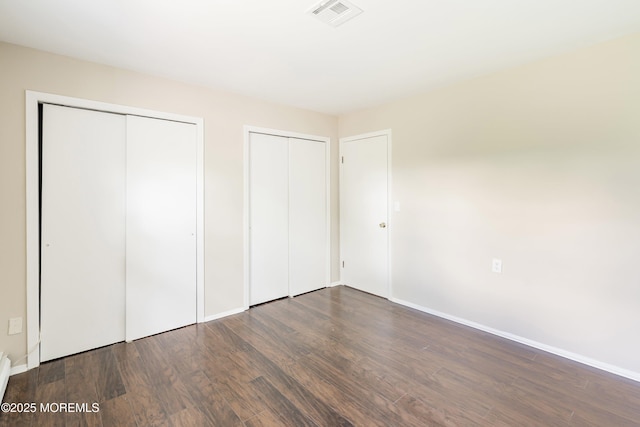 unfurnished bedroom featuring two closets, wood finished floors, baseboards, and a baseboard radiator