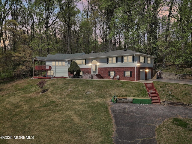 view of front of home with driveway, an attached garage, brick siding, a front lawn, and view of wooded area