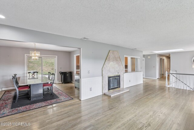 living room with wood finished floors, a textured ceiling, a chandelier, a glass covered fireplace, and a baseboard heating unit