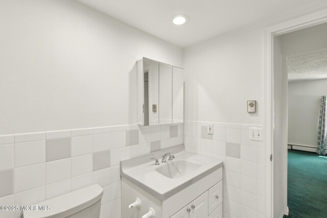 bathroom featuring toilet, tile walls, vanity, a baseboard heating unit, and wainscoting