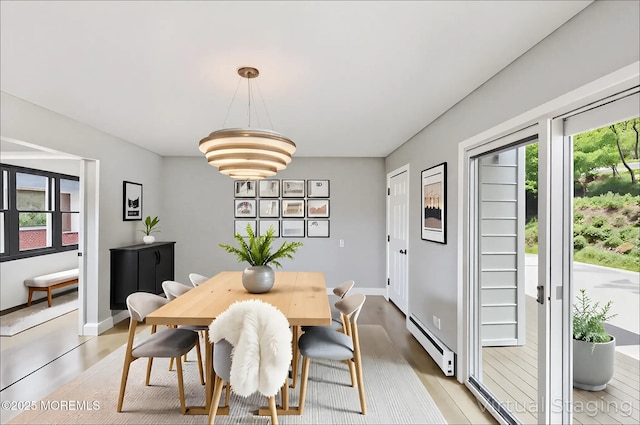 dining area featuring a baseboard heating unit, healthy amount of natural light, and light wood-style floors