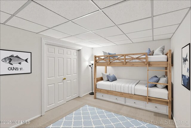 carpeted bedroom featuring a paneled ceiling, baseboards, and a closet