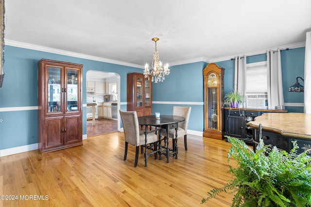 dining area featuring arched walkways, a chandelier, light wood-style flooring, baseboards, and ornamental molding