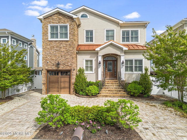 view of front of home featuring a standing seam roof, fence, an attached garage, and decorative driveway