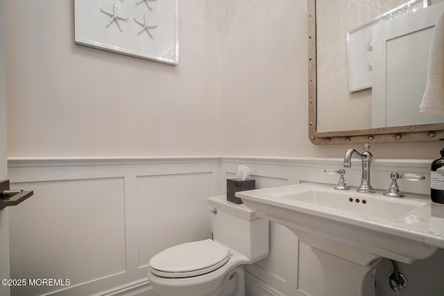 bathroom featuring a decorative wall, toilet, a wainscoted wall, and a sink