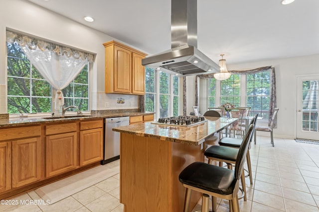 kitchen with island exhaust hood, appliances with stainless steel finishes, light tile patterned flooring, dark stone counters, and a kitchen bar