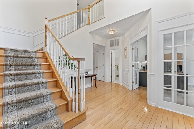 entryway featuring a decorative wall, stairway, wood-type flooring, and a wainscoted wall