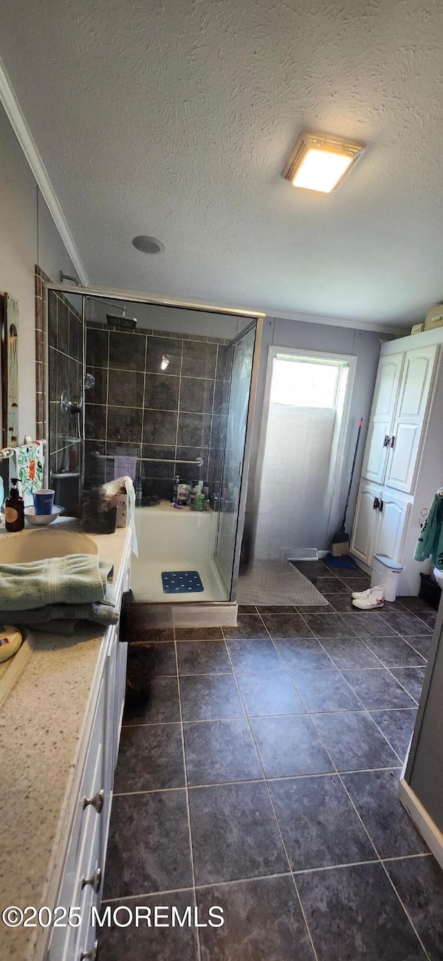 full bath with a stall shower, vanity, a textured ceiling, ornamental molding, and tile patterned floors