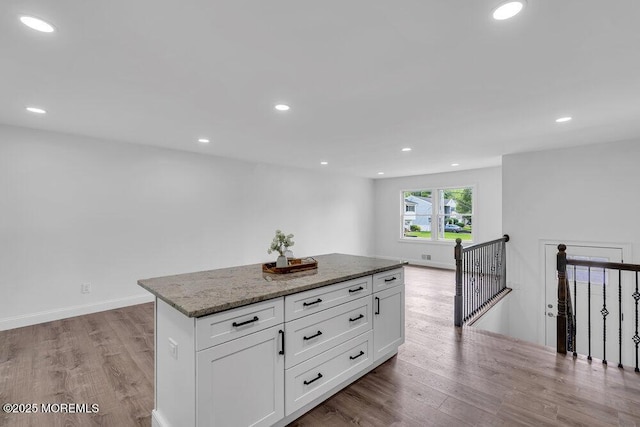 kitchen featuring light wood-style flooring, a kitchen island, stone countertops, white cabinetry, and recessed lighting