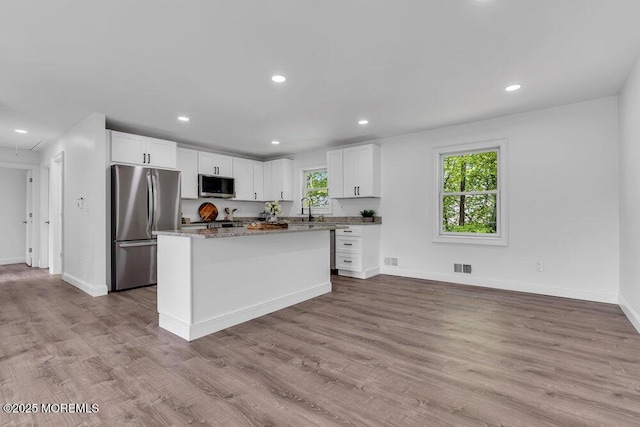 kitchen with appliances with stainless steel finishes, a sink, white cabinetry, baseboards, and wood finished floors