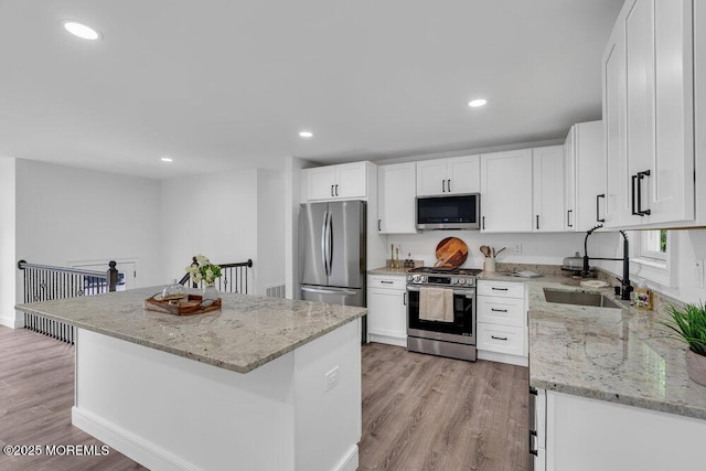 kitchen featuring appliances with stainless steel finishes, a sink, white cabinetry, light wood-style floors, and recessed lighting