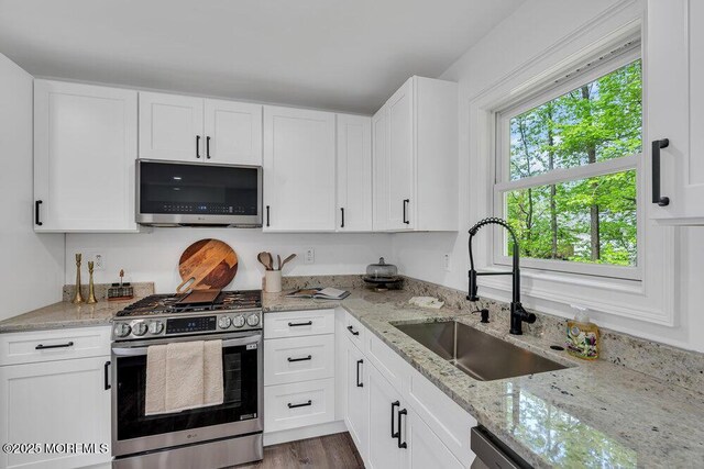 kitchen featuring stainless steel appliances, a sink, white cabinetry, and light stone countertops