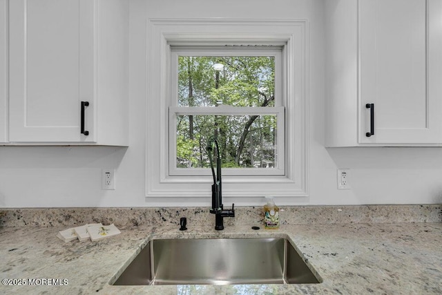 kitchen view of a sink, white cabinetry, and light stone counters