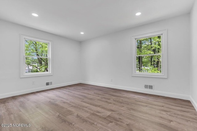 unfurnished room with healthy amount of natural light, wood finished floors, baseboards, and recessed lighting