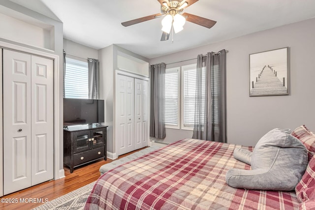 bedroom with two closets, wood finished floors, a ceiling fan, and a baseboard heating unit