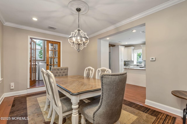 dining room featuring washer / clothes dryer, a chandelier, plenty of natural light, wood finished floors, and crown molding