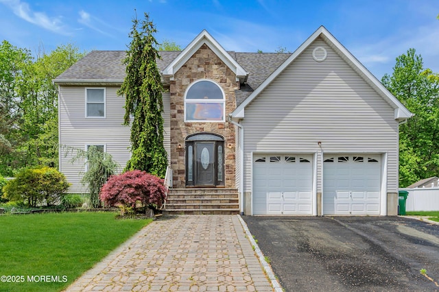 traditional-style home with driveway, a front yard, an attached garage, stone siding, and a shingled roof