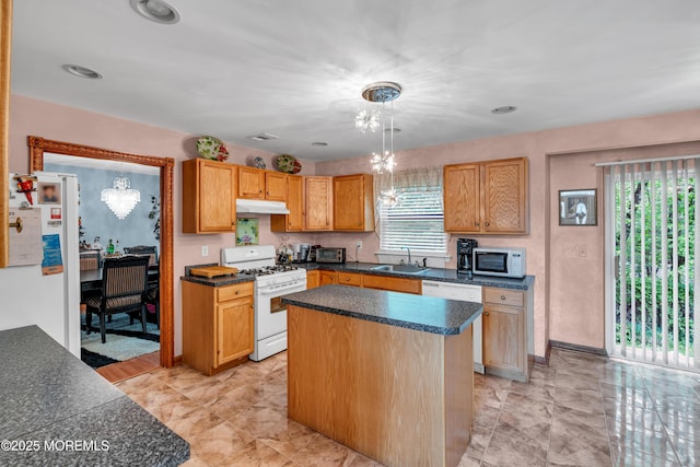 kitchen featuring white appliances, under cabinet range hood, a sink, dark countertops, and pendant lighting
