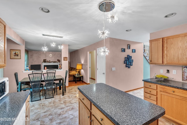 kitchen featuring dark countertops, a chandelier, a center island, open floor plan, and a fireplace