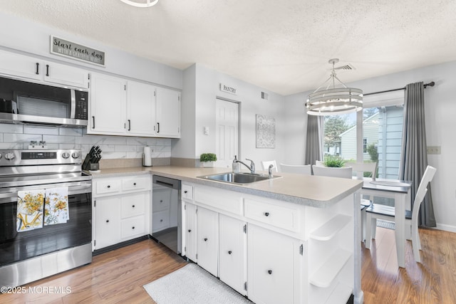 kitchen with appliances with stainless steel finishes, a textured ceiling, a sink, a peninsula, and light countertops