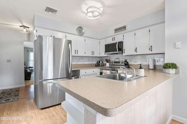 kitchen featuring appliances with stainless steel finishes, a peninsula, a sink, tasteful backsplash, and a textured ceiling