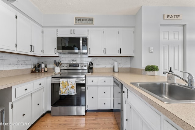 kitchen featuring appliances with stainless steel finishes, a sink, light countertops, white cabinets, and a textured ceiling