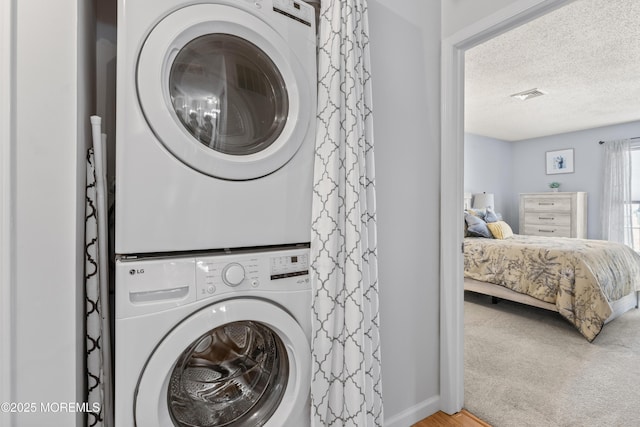 laundry room featuring stacked washer / drying machine, a textured ceiling, baseboards, and wood finished floors
