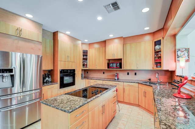 kitchen with black appliances, light brown cabinetry, a sink, dark stone counters, and backsplash