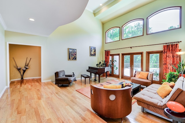 living area with french doors, a towering ceiling, wood finished floors, baseboards, and ornamental molding