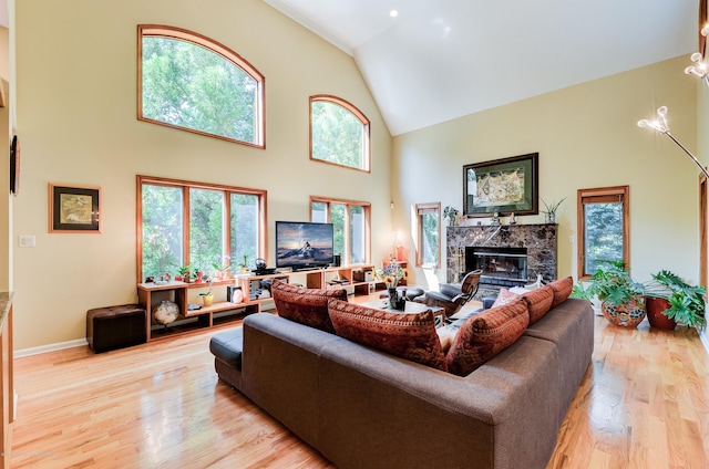 living area with a high end fireplace, high vaulted ceiling, light wood-type flooring, and baseboards