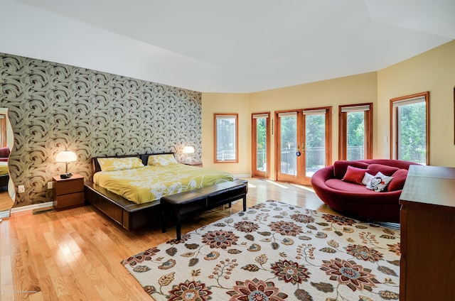 bedroom featuring wallpapered walls, access to exterior, an accent wall, french doors, and light wood finished floors