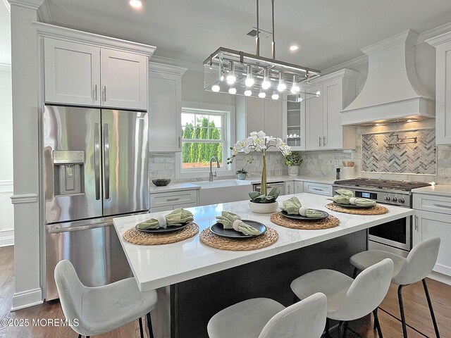 kitchen featuring appliances with stainless steel finishes, premium range hood, white cabinets, light countertops, and a sink