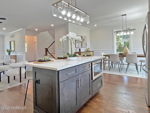 kitchen with gray cabinetry, crown molding, a center island, wood finished floors, and freestanding refrigerator