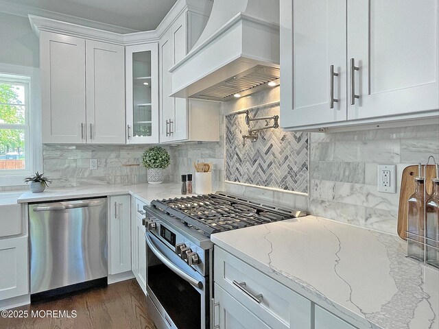 kitchen with appliances with stainless steel finishes, premium range hood, white cabinetry, and light stone counters