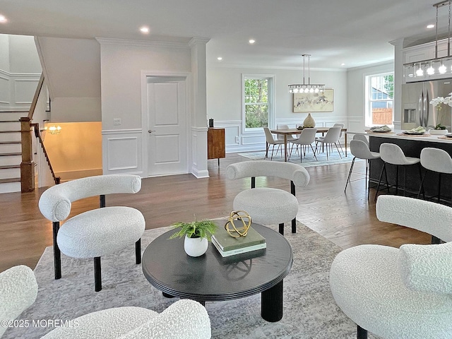 living room with wood finished floors, healthy amount of natural light, stairs, ornamental molding, and a wainscoted wall