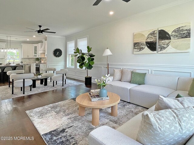 living area featuring a ceiling fan, wood finished floors, ornamental molding, recessed lighting, and a wainscoted wall