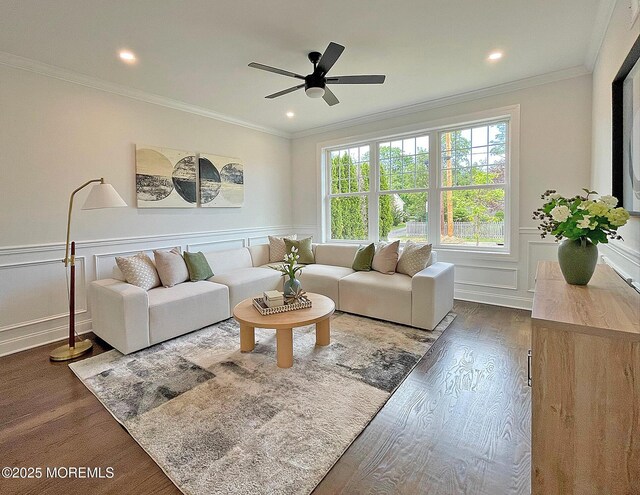 living room featuring wood finished floors, ceiling fan, crown molding, a decorative wall, and a wainscoted wall