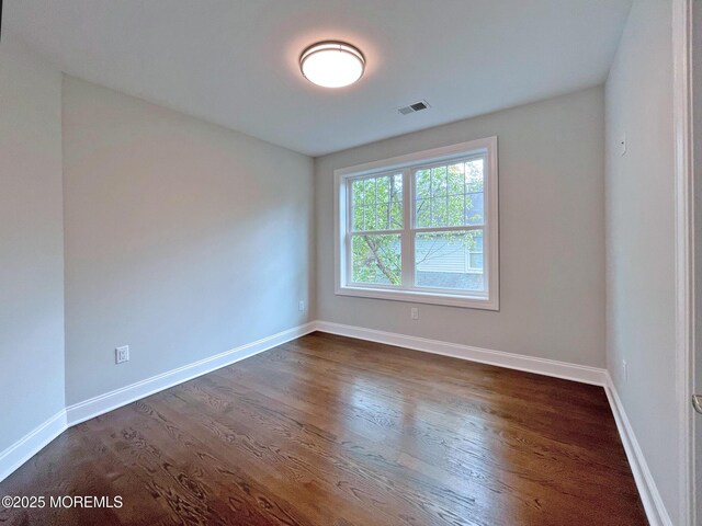 spare room featuring dark wood-style floors and baseboards
