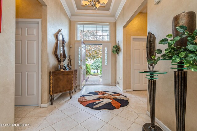 foyer featuring crown molding, a chandelier, light tile patterned floors, baseboards, and a textured wall